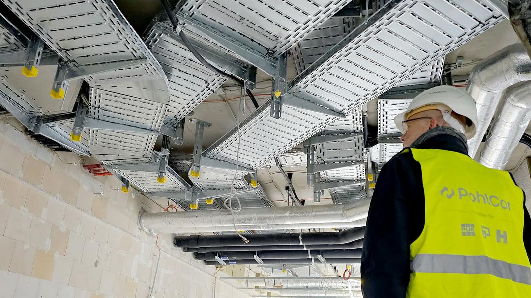 Monteur mit PohlCon-Weste prüft installierte Kabeltrassen und Leitungen unter der Decke in einer Tiefgarage.