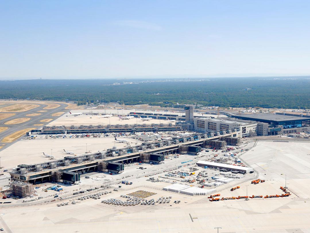 Luftaufnahme des Flughafen-Terminalbaus mit Rollfeldern, Flugzeugen, Gebäuden und umliegendem Waldgebiet